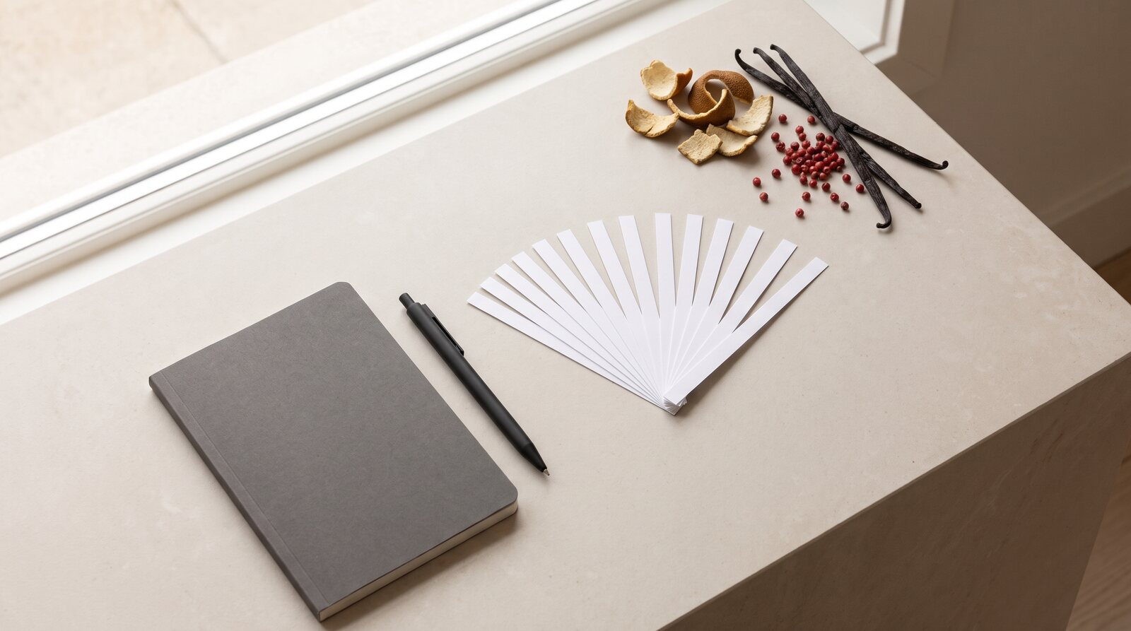 Bright work surface with a fan of smelling strips, a notebook, a pen and raw materials